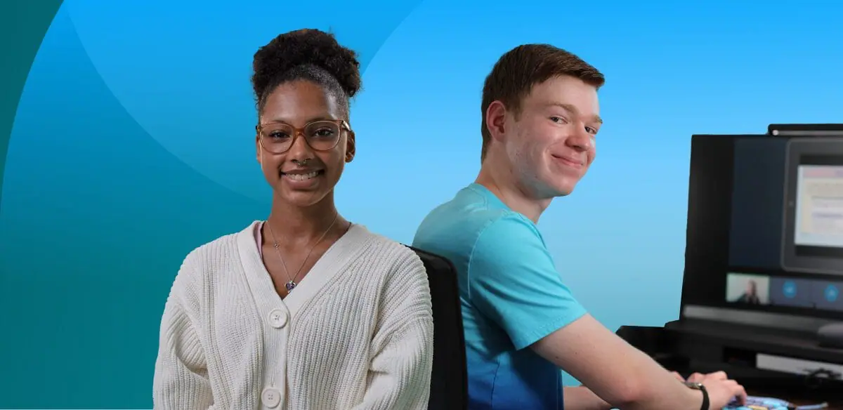 A girl smiling at the camera wearing glasses and a boy sitting at their computer